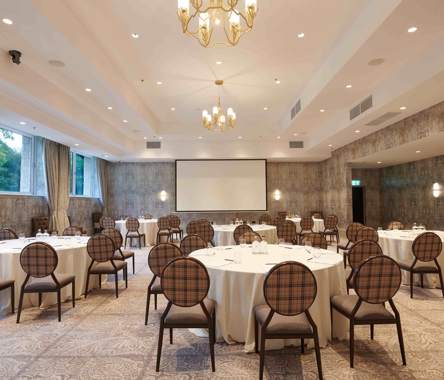 Event space with plenty of tables and seating along with a projector screen and chandelier lighting