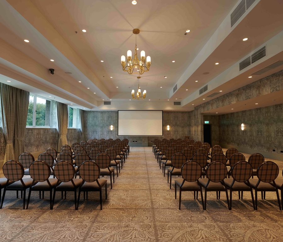 Meeting space inside Cameron House with rows of seating, large projector screen and channeller lighting