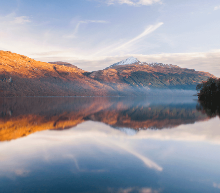 a picture taken from the edge of water showing some large mountains in the back