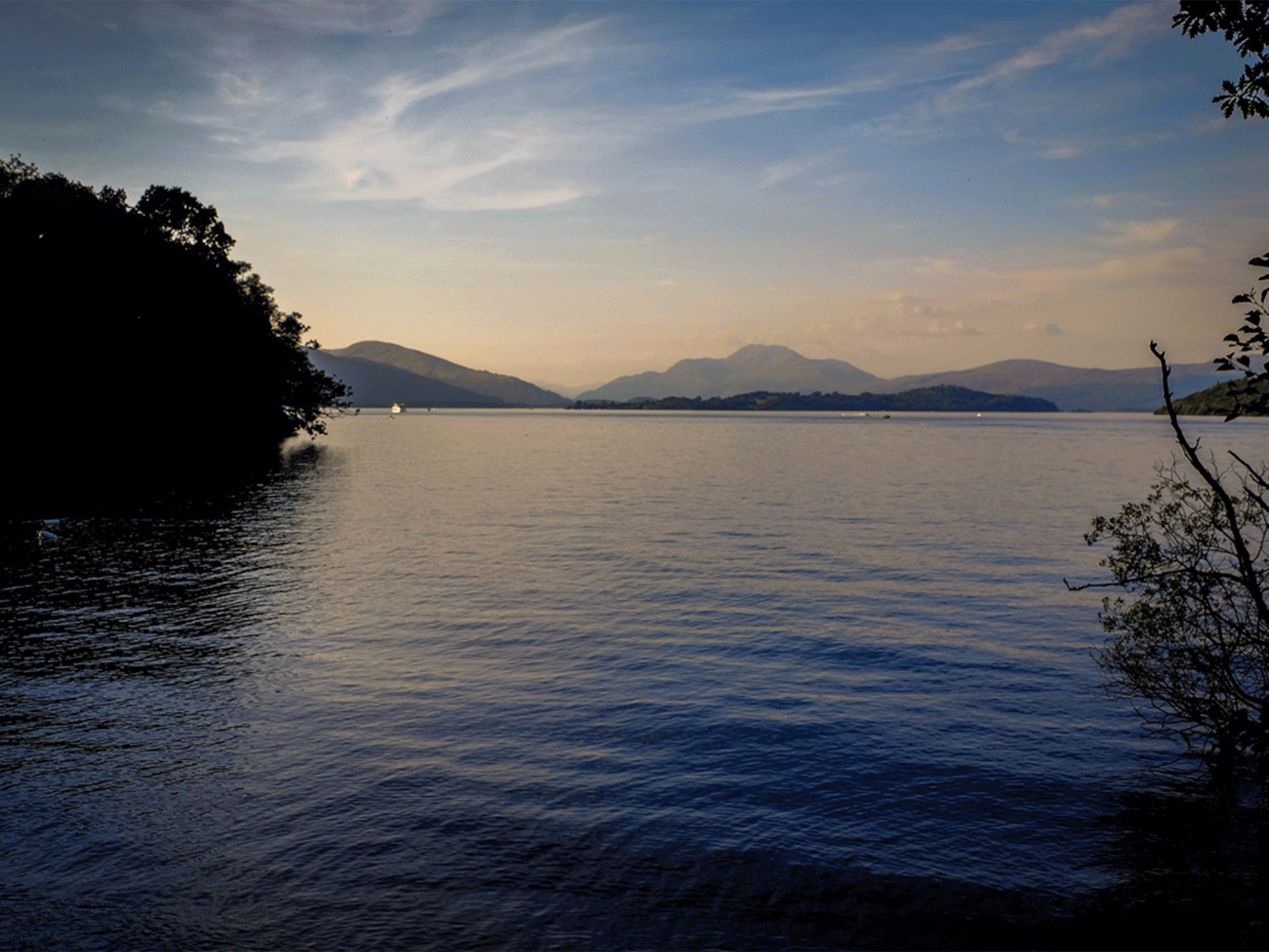 large body of water with mountains in the far background and the sun setting