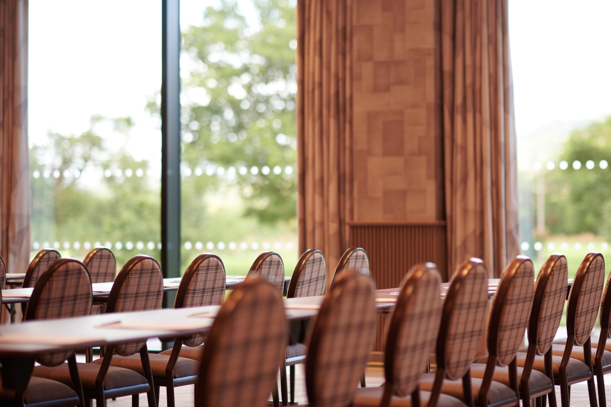 close up view of chairs and tables set up inside an event space with a view of the massive green trees outside