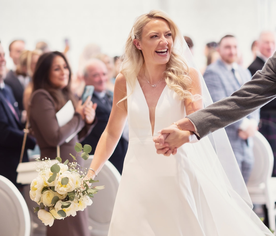 a bride and groom smiling and walking down the aisle amongst their wedding guests.