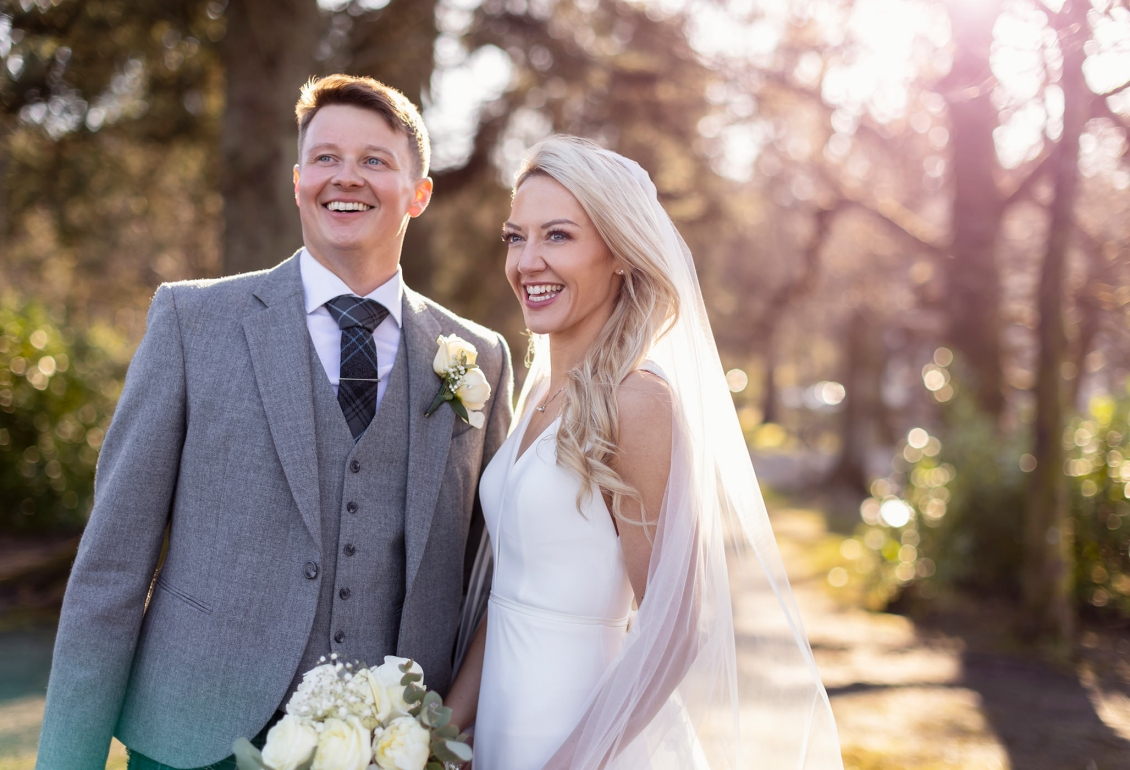 a bride and groom standing outside on a sunny day smiling