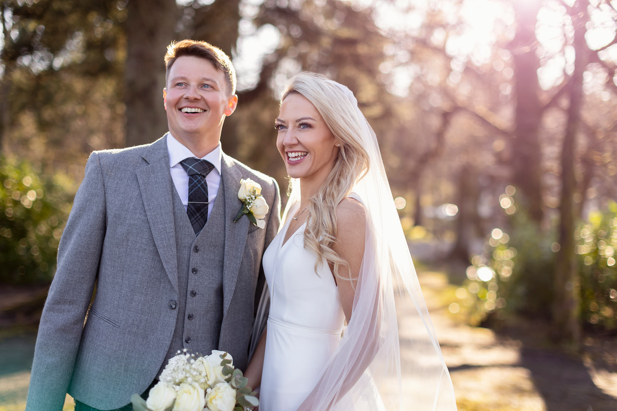 a bride and groom standing outside on a sunny day smiling