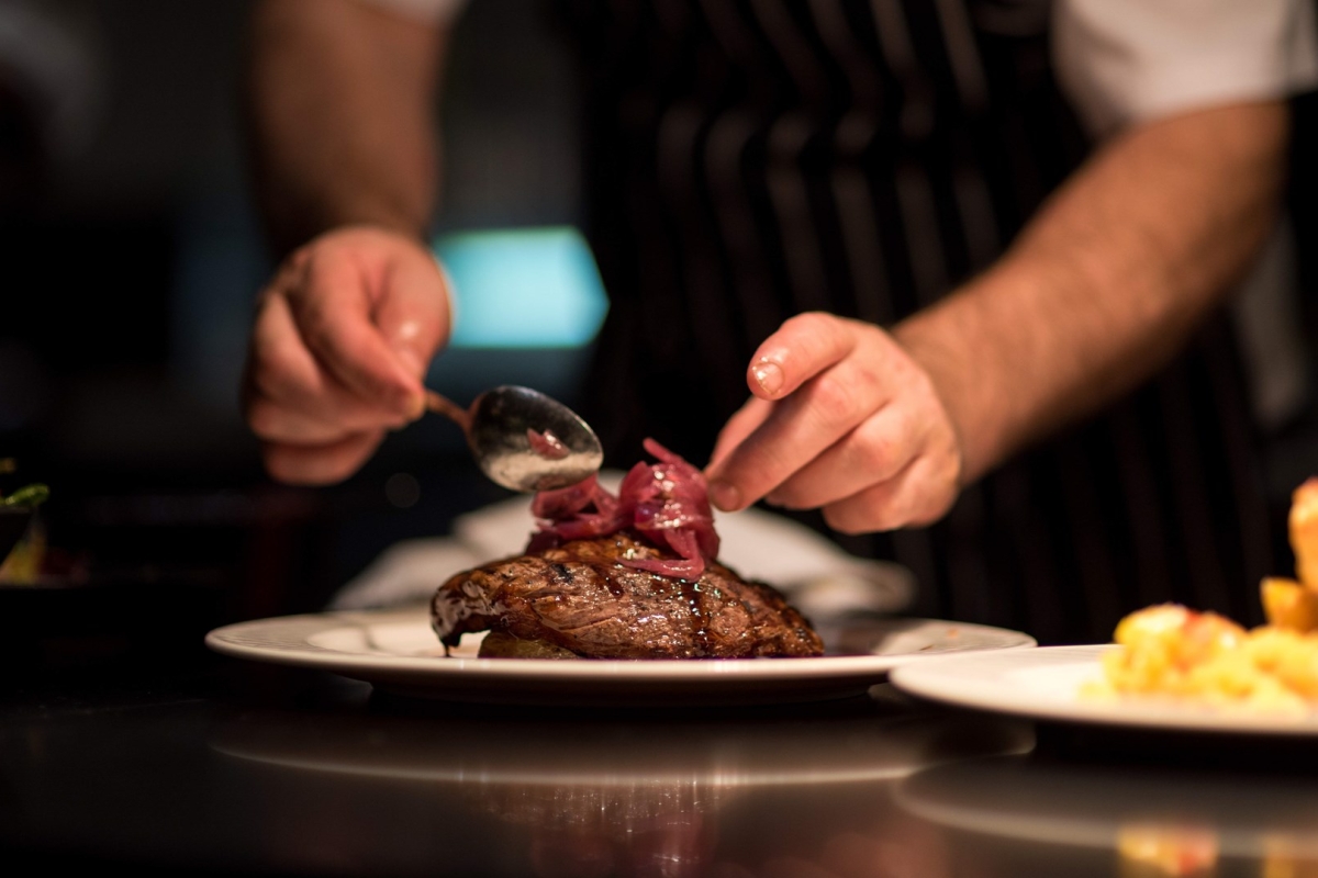 a chef preparing a piece of meat by placing garnish on the top