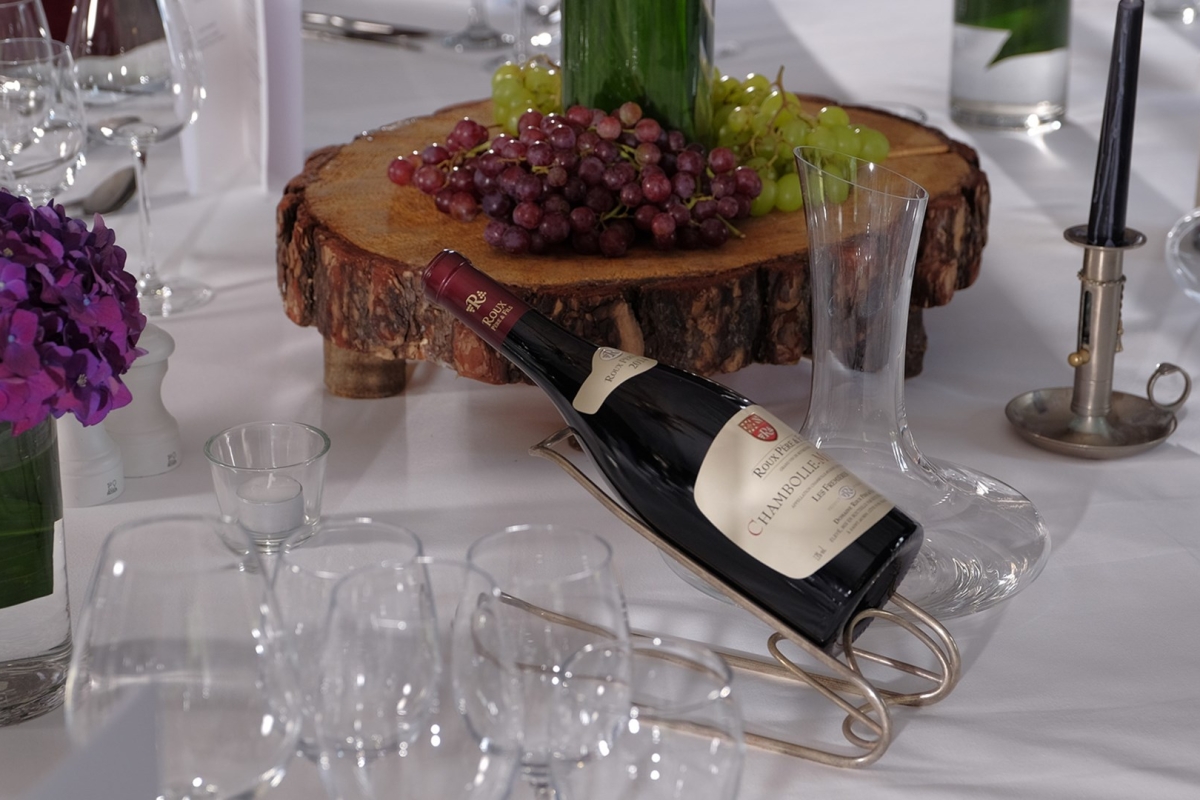 a bottle of wine sitting on a stand on a table with a center piece in the middle