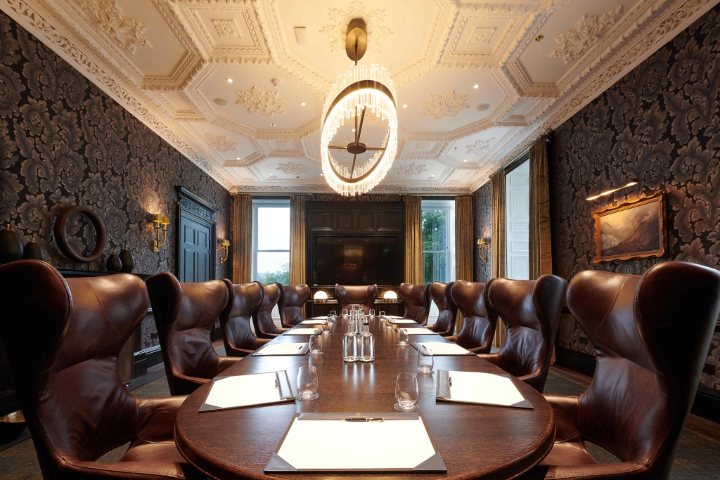 Large round table surrounded by brown leather chairs and a large lighting fixture above