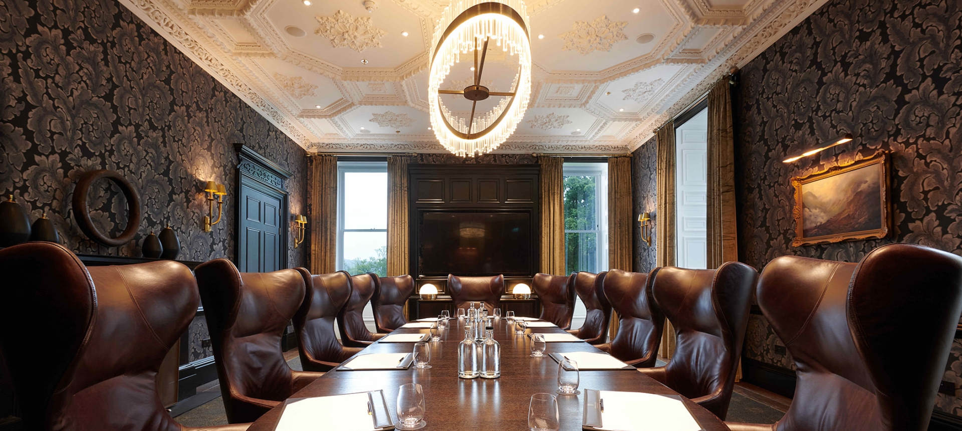 Large round table surrounded by brown leather chairs and a large lighting fixture above