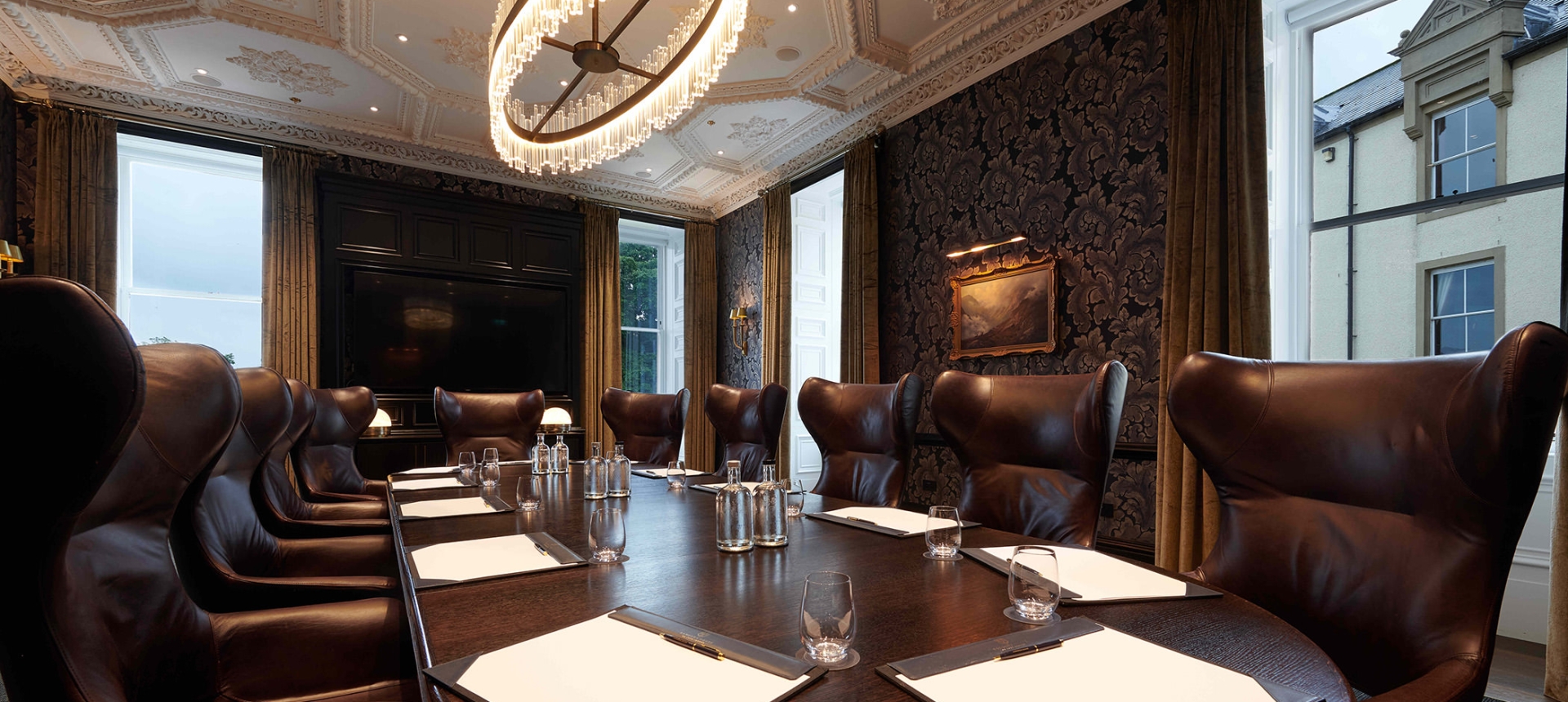 Large oval table and brown chairs with windows looking outside to the exterior of the building