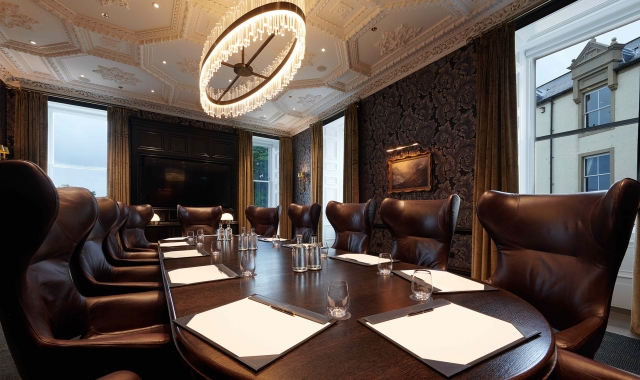 Large oval table and brown chairs with windows looking outside to the exterior of the building