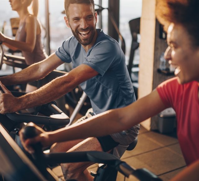 a man and a woman smiling while riding exercises bikes