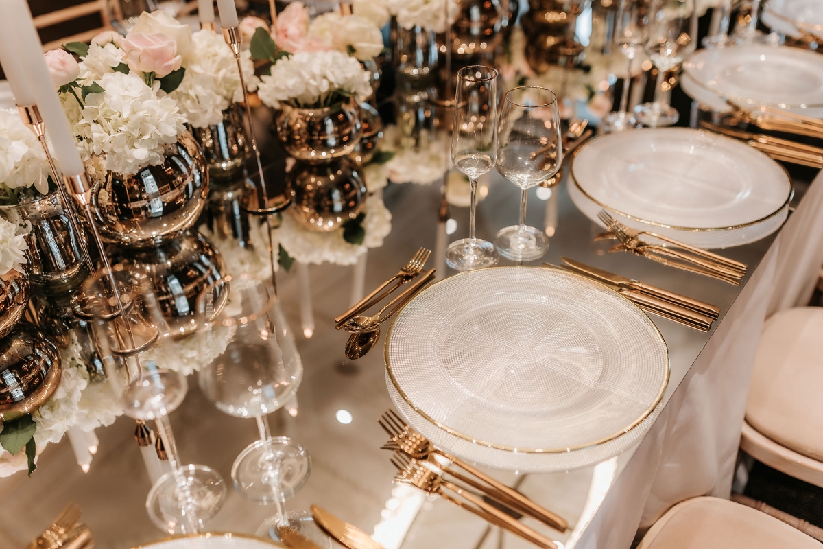 elegant dining arrangement with gold silverware paired with flowers and candles on the center of the table