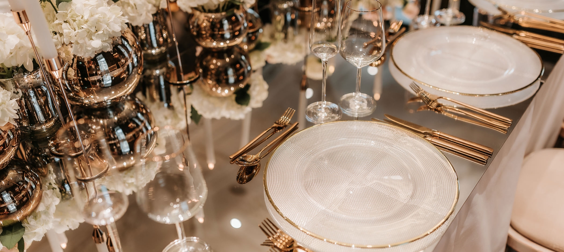 elegant dining arrangement with gold silverware paired with flowers and candles on the center of the table