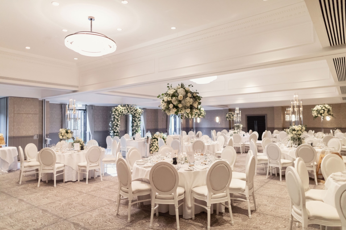 a large wedding area with white tables and chairs with floral arrangements standing tall on top of the tables