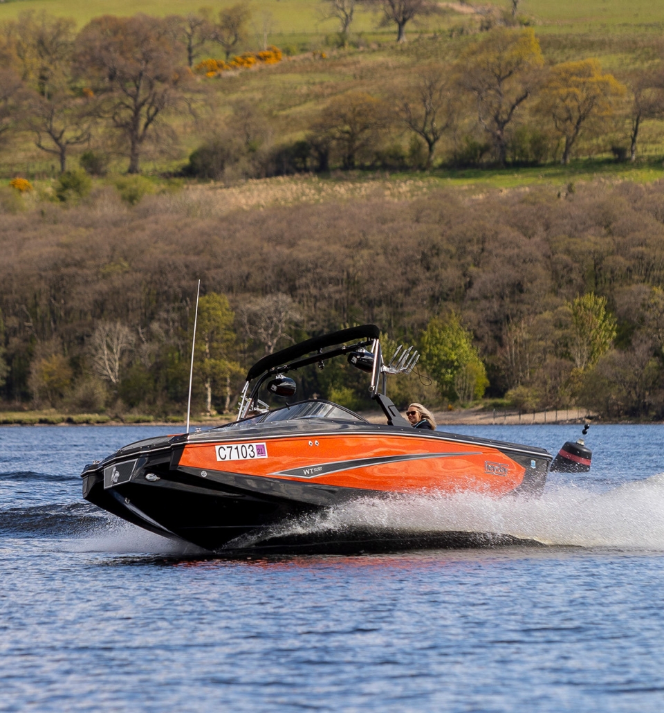 people riding in a black and orange boat in the middle of the water with trees in the background