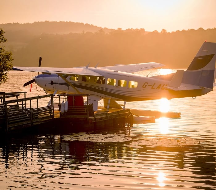 a white and blue plane sitting on the water with the sun setting behind it