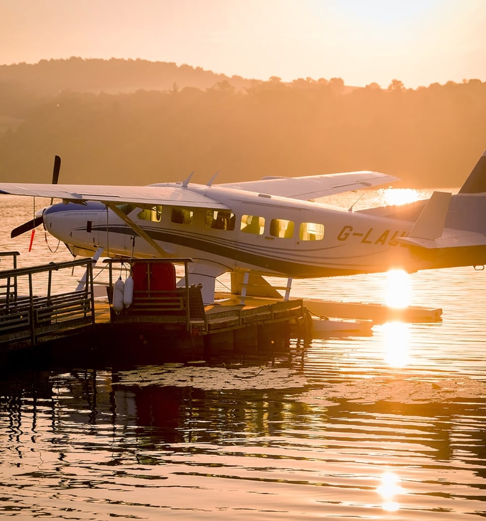a white and blue plane sitting on the water with the sun setting behind it