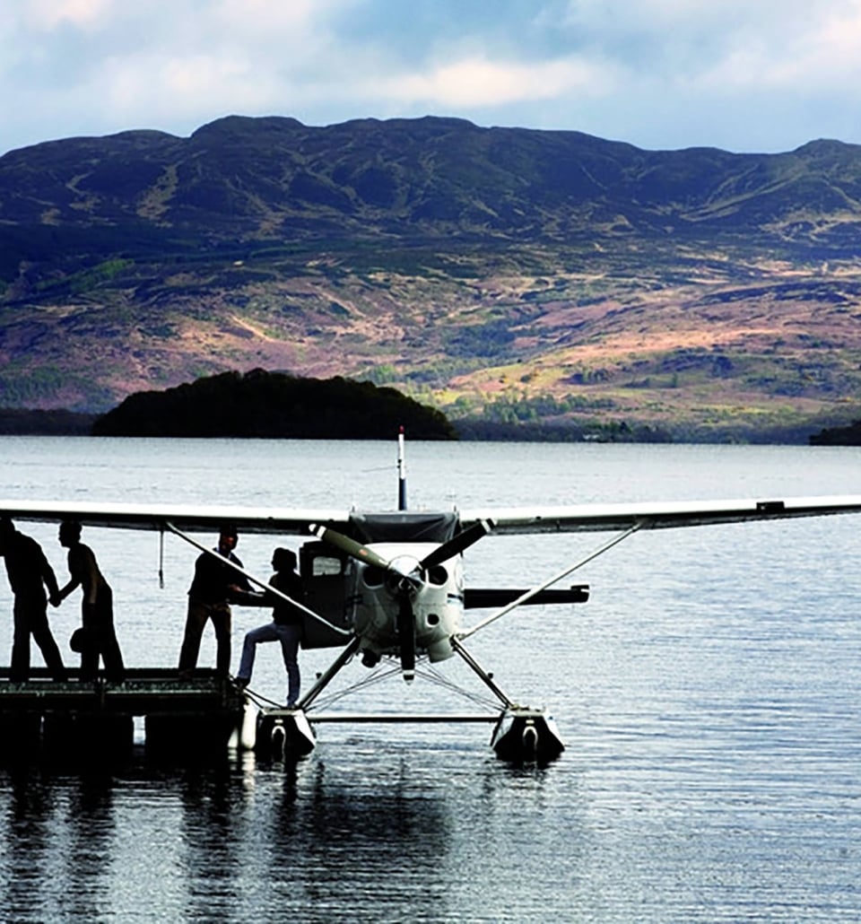 people stepping out of a plane sitting on the water docked with mountains in the background