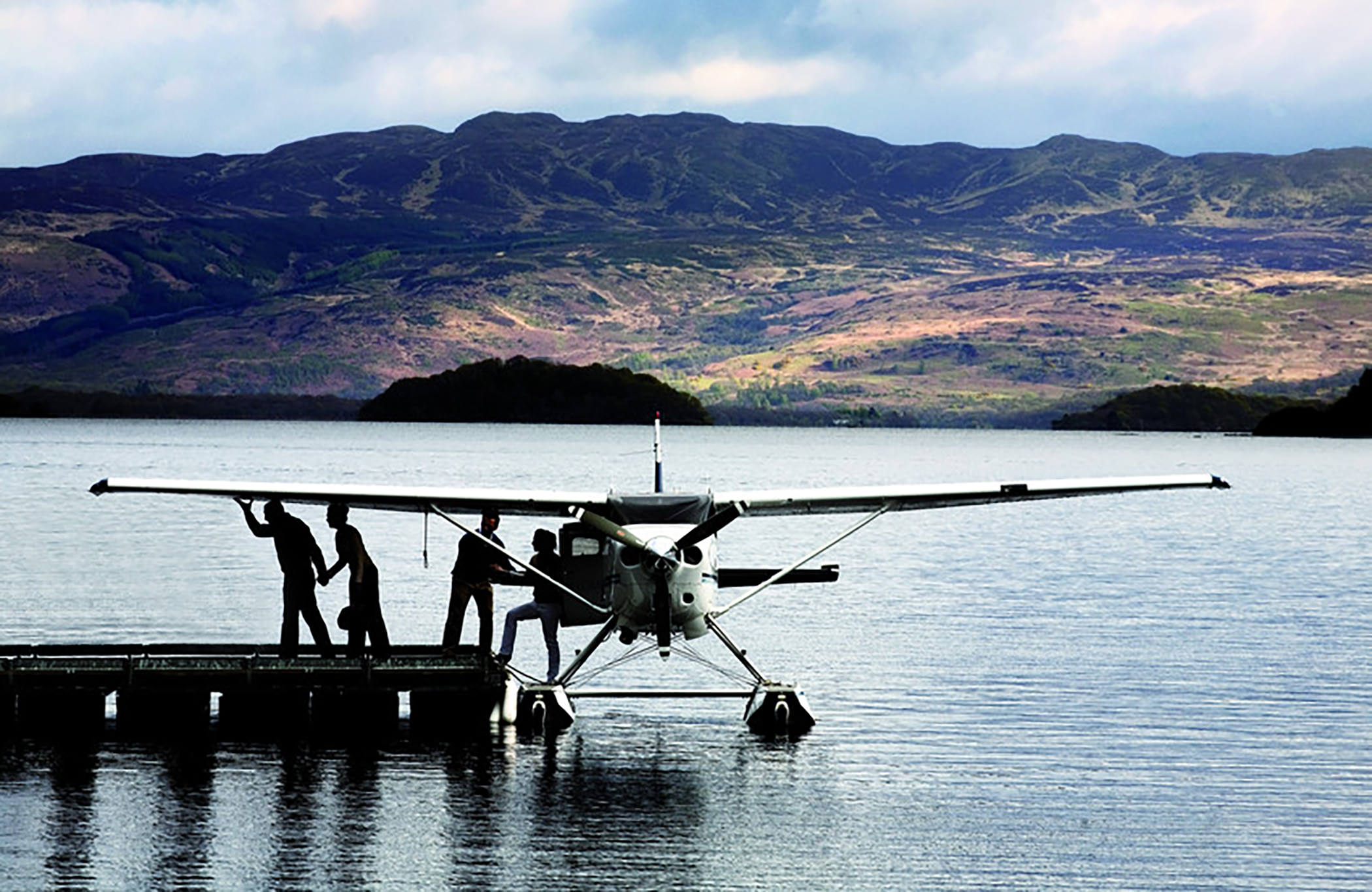 people stepping out of a plane sitting on the water docked with mountains in the background