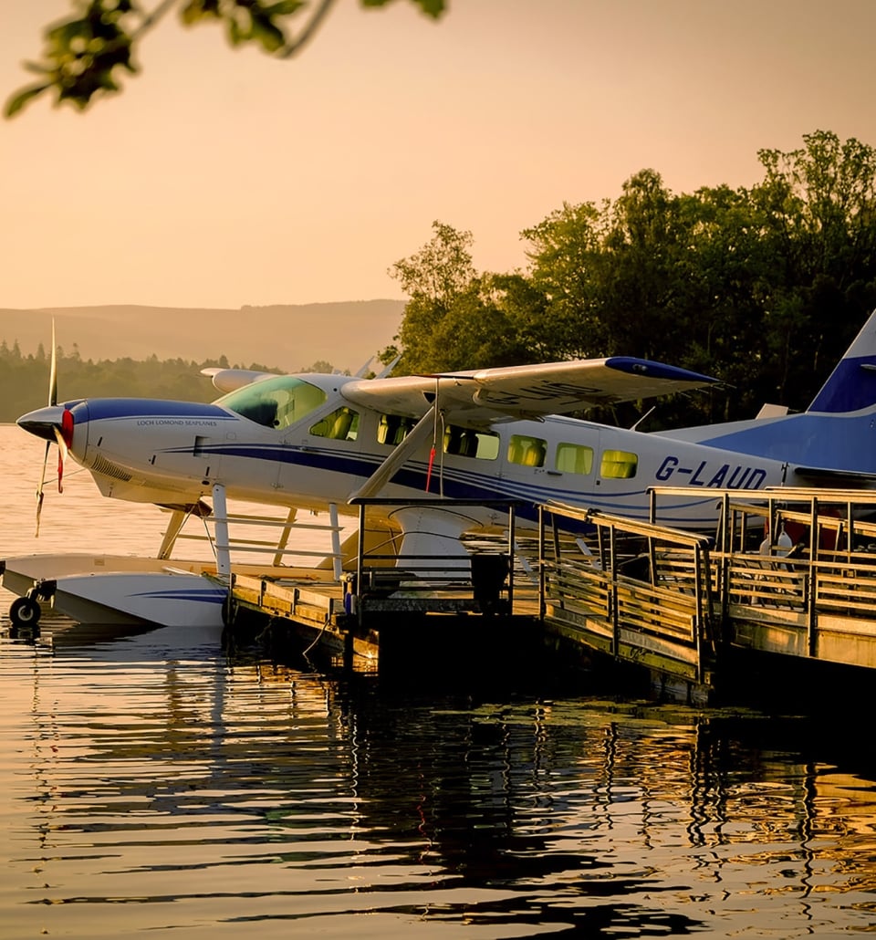 a sea plane sitting on the water tied to a dock with the sun setting behind it