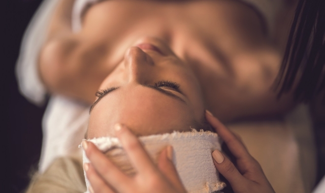 a woman laying under a towel having her head patted with a rag