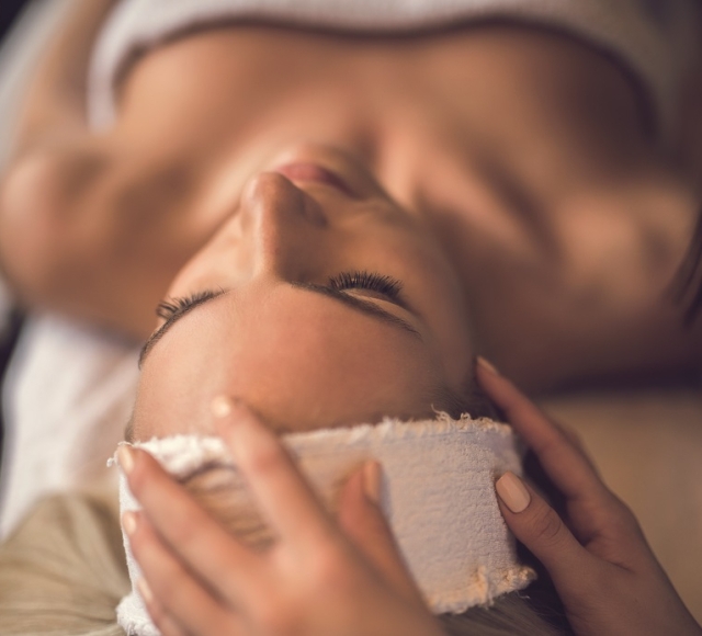 a woman laying under a towel having her head patted with a rag