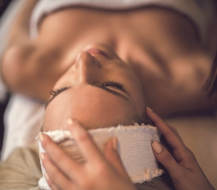 a woman laying under a towel having her head patted with a rag