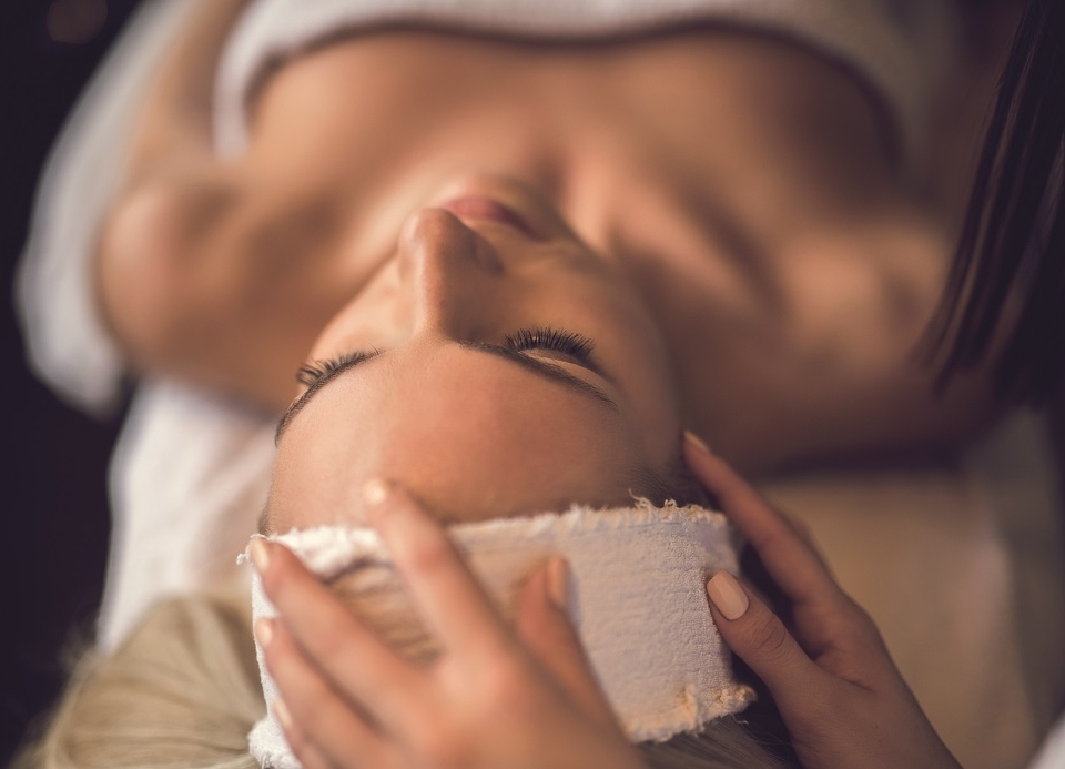 a woman laying under a towel having her head patted with a rag