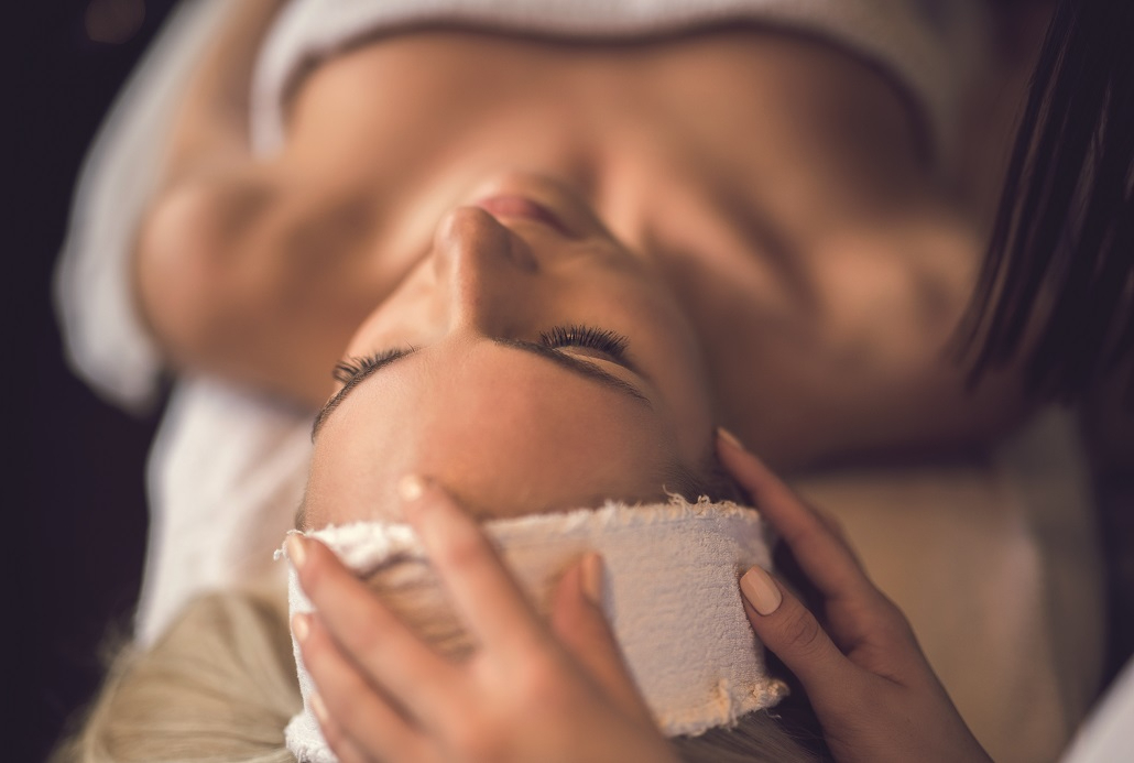 a woman laying under a towel having her head patted with a rag