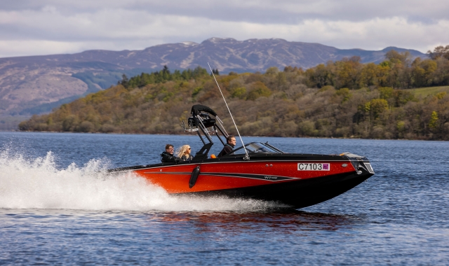 a red and black boat with people on board driving across the open body of water