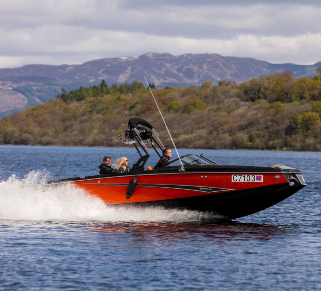 a red and black boat with people on board driving across the open body of water