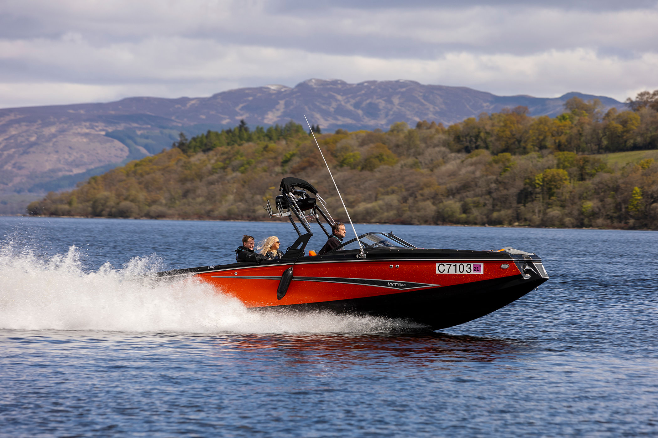 a red and black boat with people on board driving across the open body of water