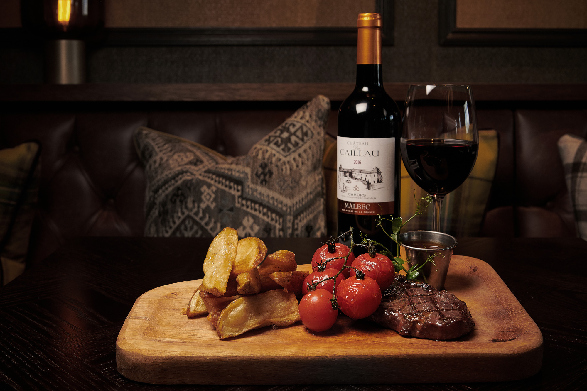 a board with steak, tomatoes, potatoes and red wine