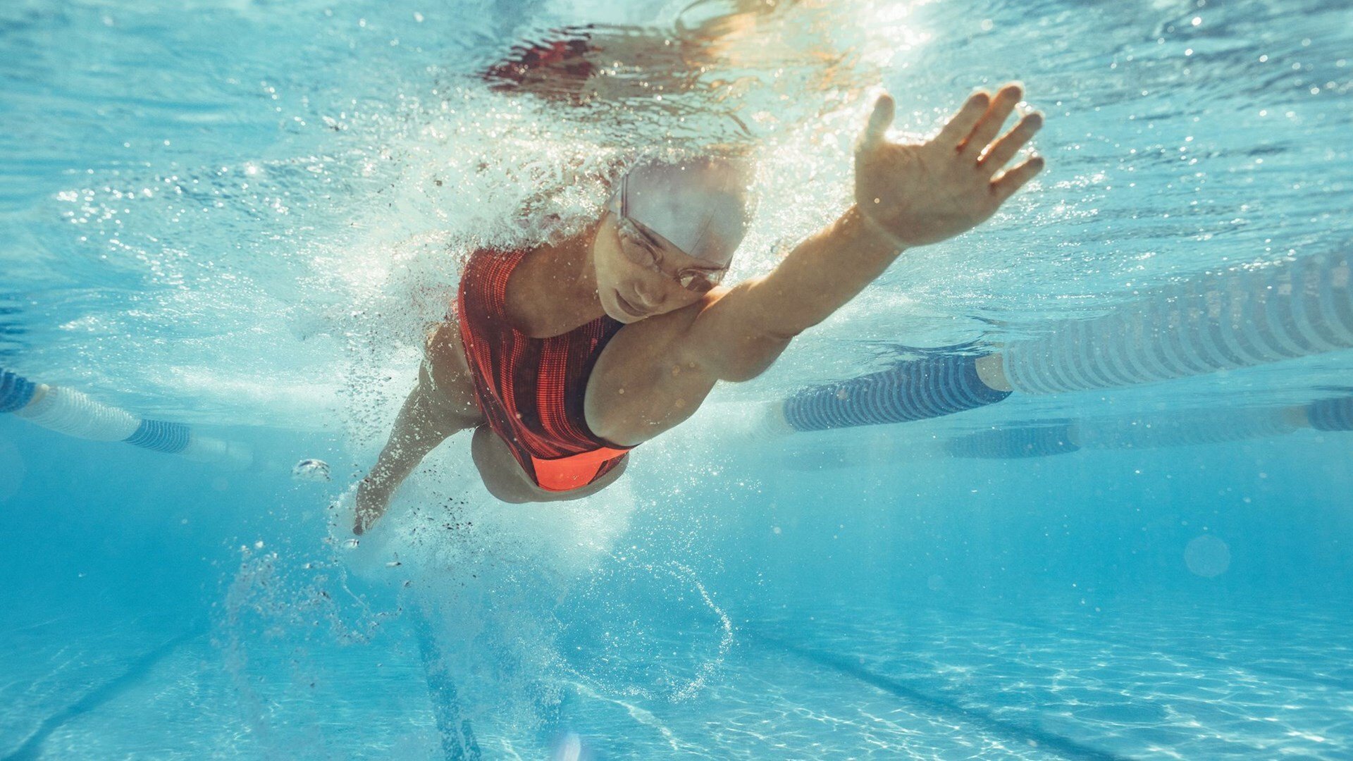 Underwater view of a swimmer in a swimming cap doing the front crawl in a pool