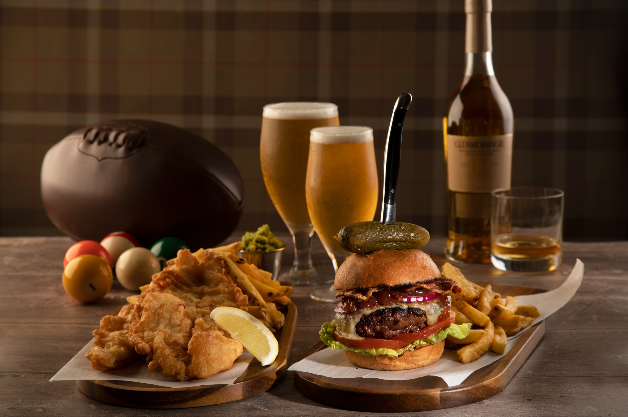 fish and chips paired with a burger and fries in front of some alcohol on a table