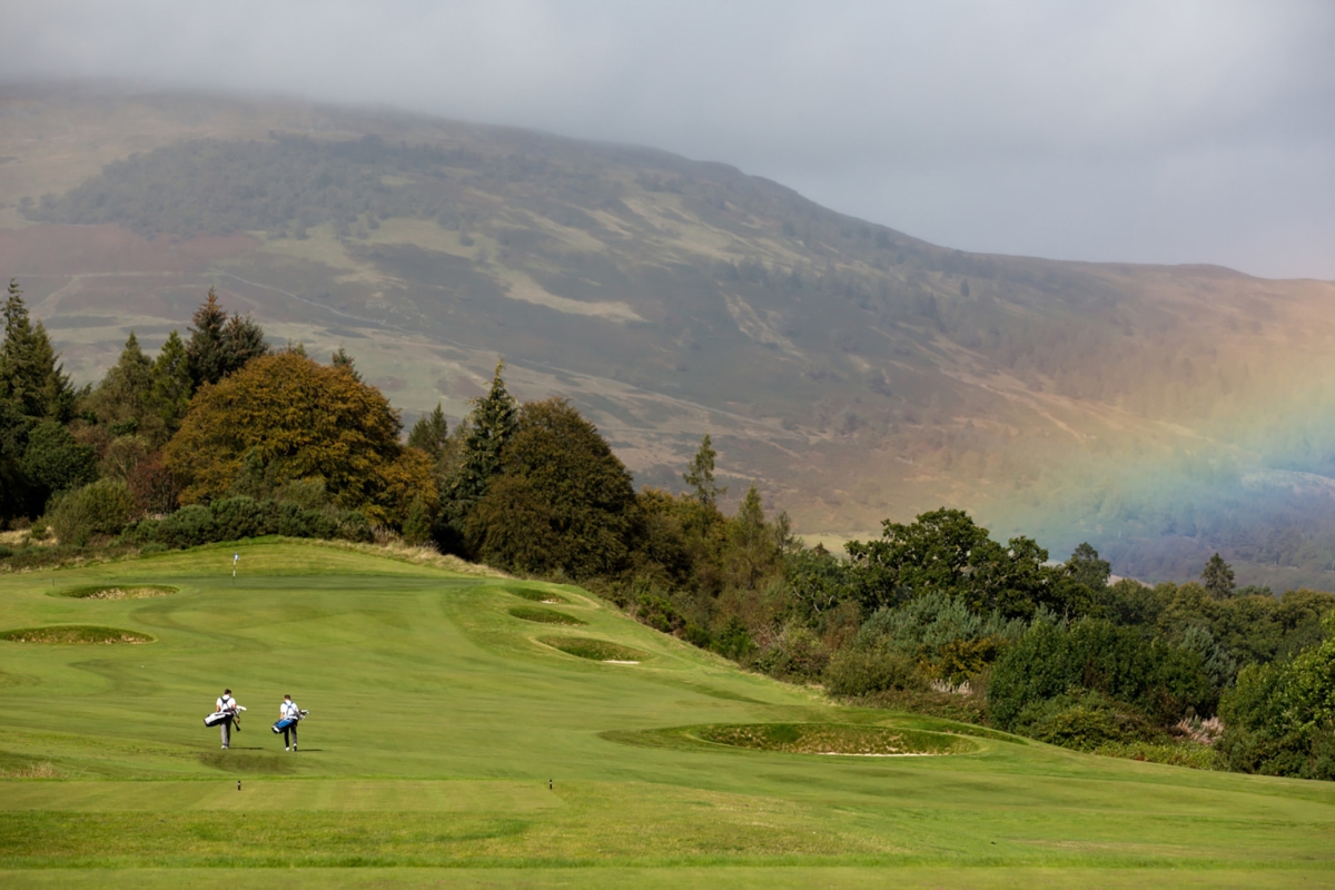 golfers playing golf on a golf course with a rainbow in the back ground