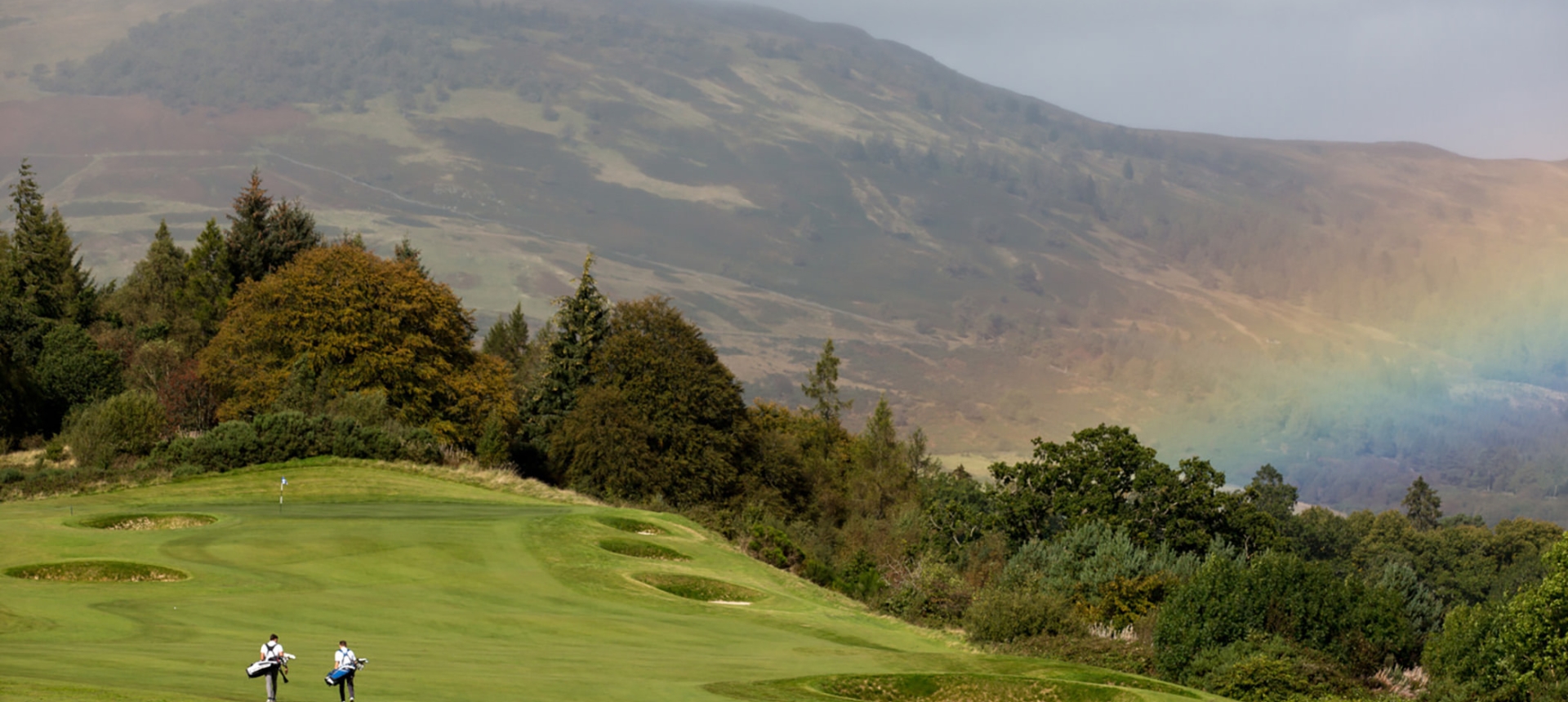 golfers playing golf on a golf course with a rainbow in the back ground