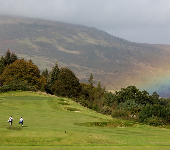 golfers playing golf on a golf course with a rainbow in the back ground