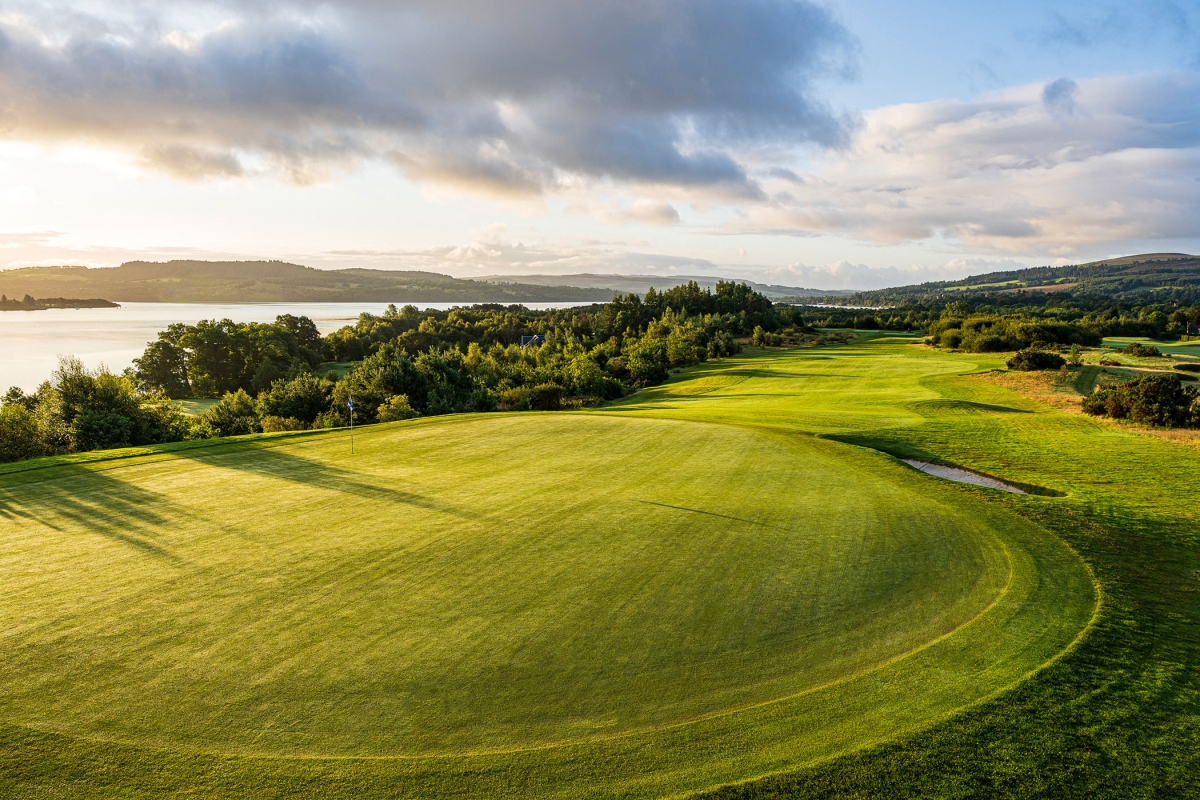 birds eye view of a golf course next to a large body of water with clouds in the sky