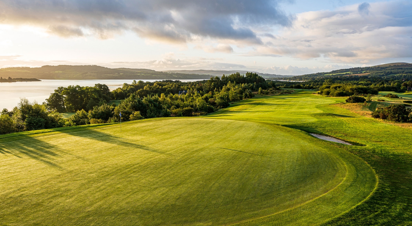 birds eye view of a golf course next to a large body of water with clouds in the sky