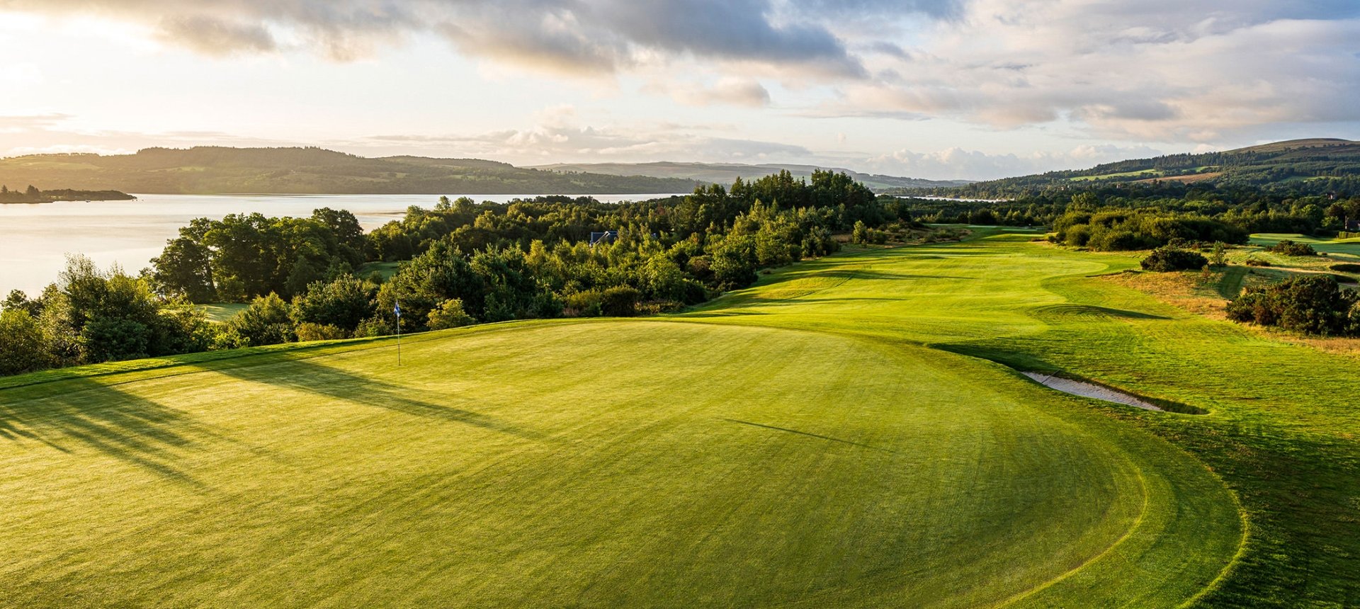 birds eye view of a golf course next to a large body of water with clouds in the sky