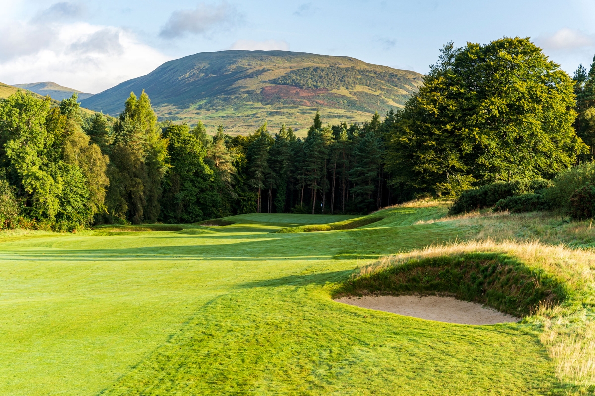 close up view of a sand pit on a golf course with trees and mountains behind