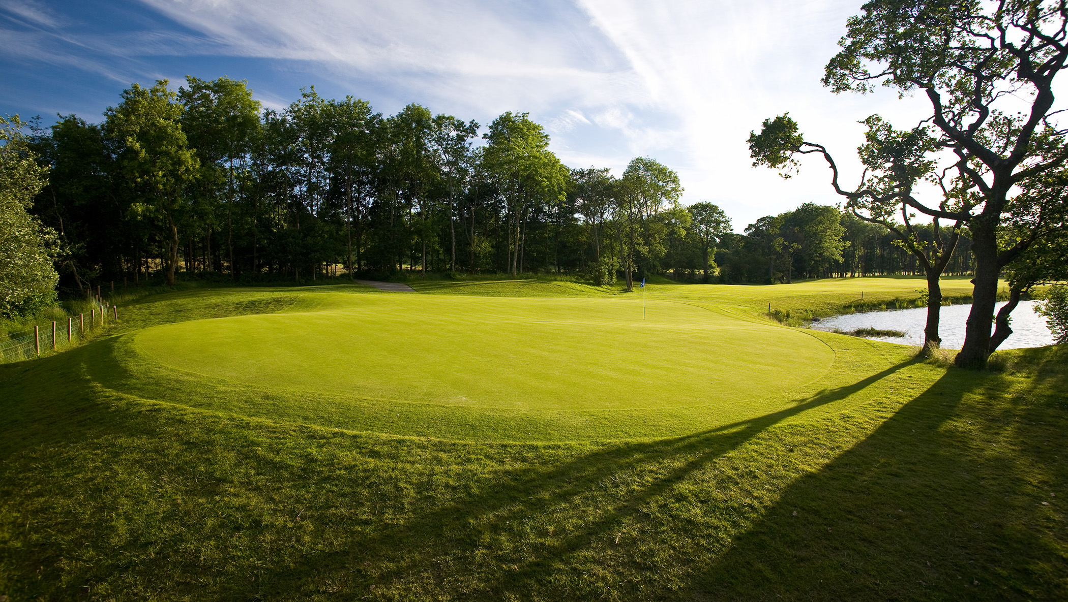 a golf course on a bright sunny day next to a small lake