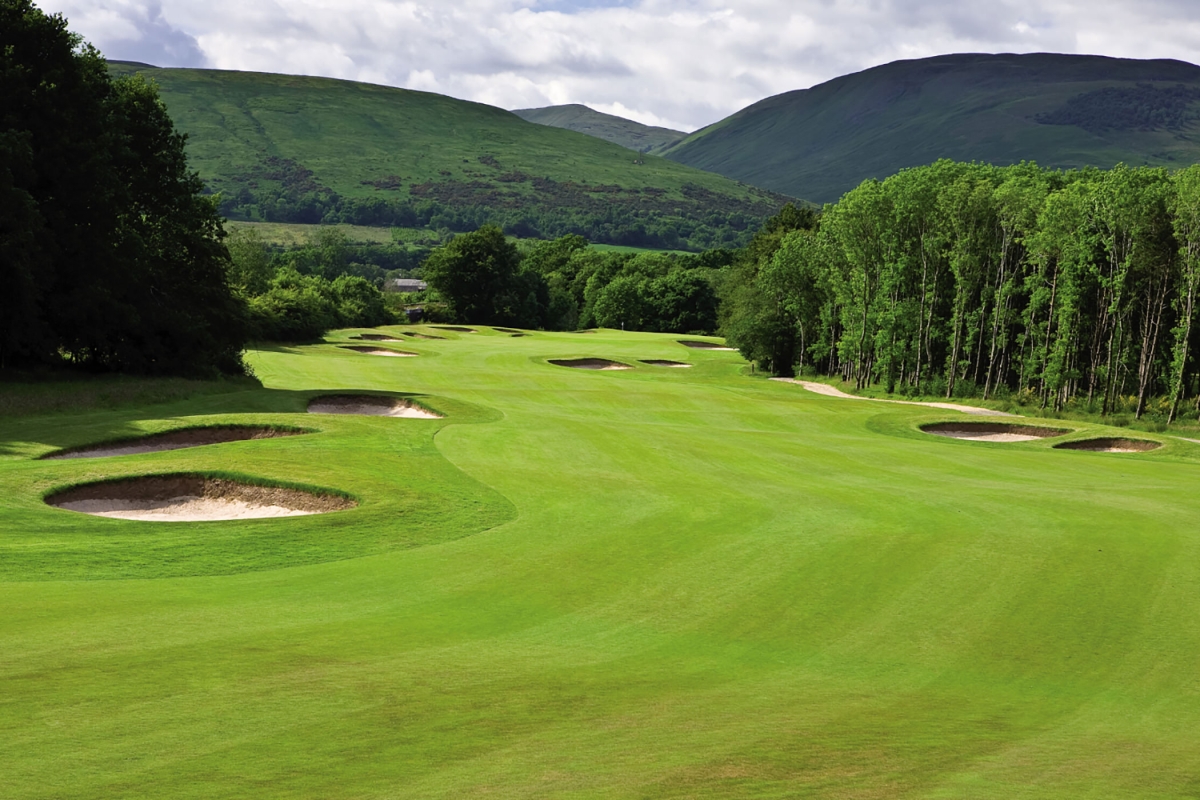 a golf course with sand pits next to forests and mountains in the back ground