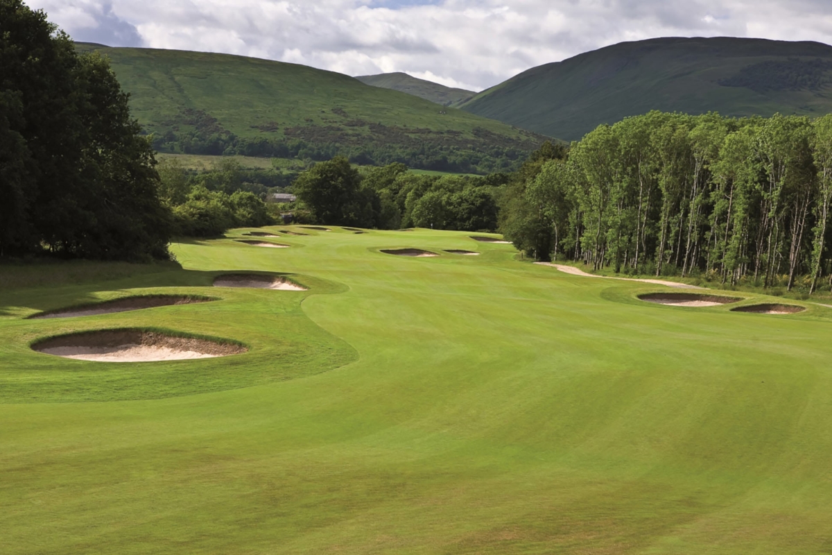 a golf course with sand dunes next to tall trees and mountains behind