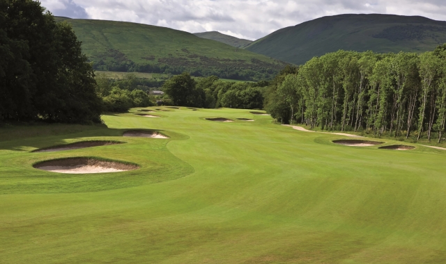 a golf course with sand dunes next to tall trees and mountains behind