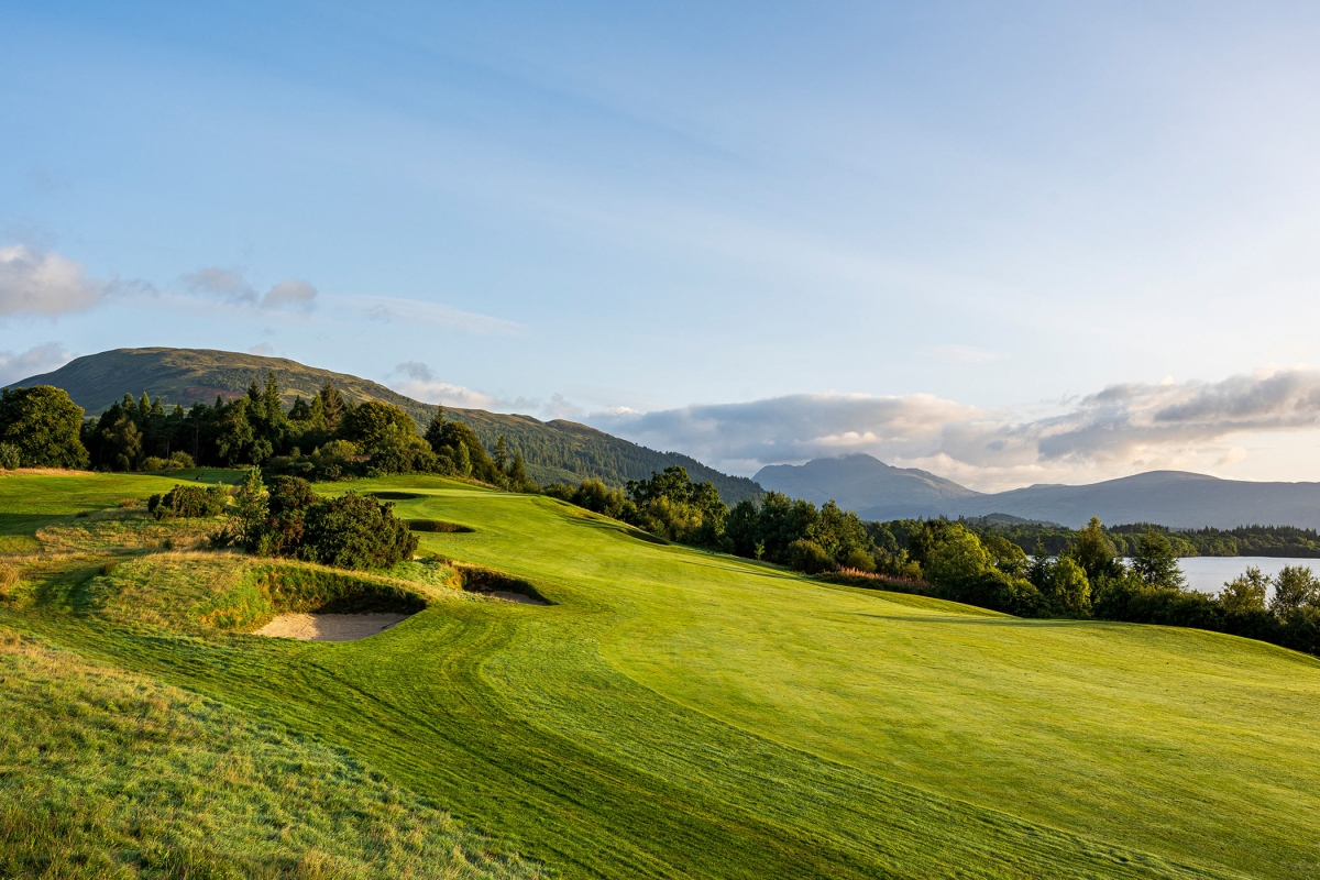 golf course going up a small hill with trees around the out side and mountains in the back ground