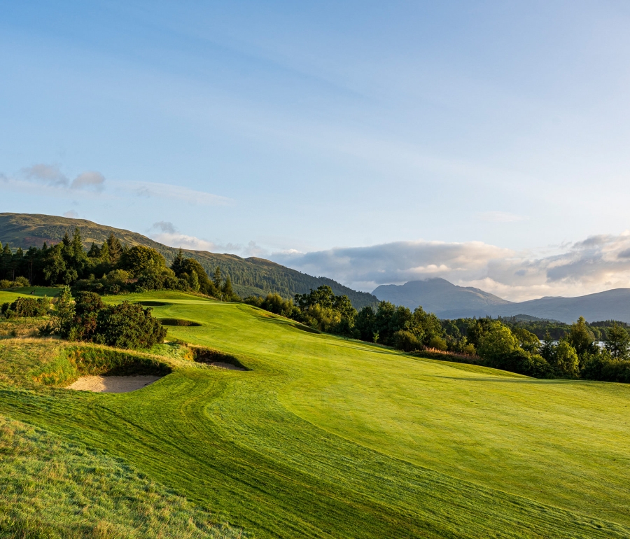 golf course going up a small hill with trees around the out side and mountains in the back ground