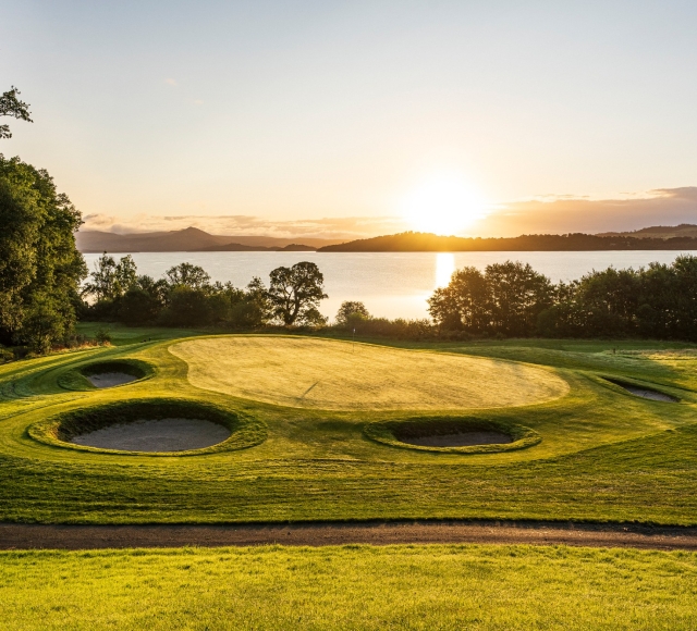 golf course with bright green grass and sand pits also the sun setting in the back