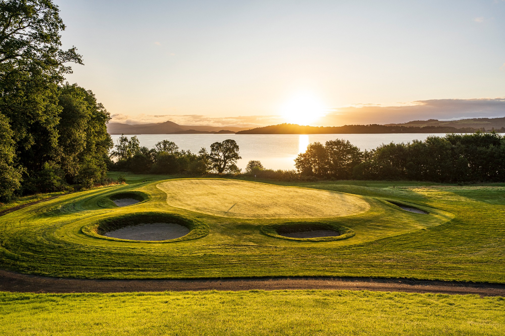 golf course with bright green grass and sand pits also the sun setting in the back